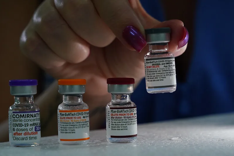 Mãos de enfermeira preparando vacina monovalente contra Covid-19 com seringa e frasco