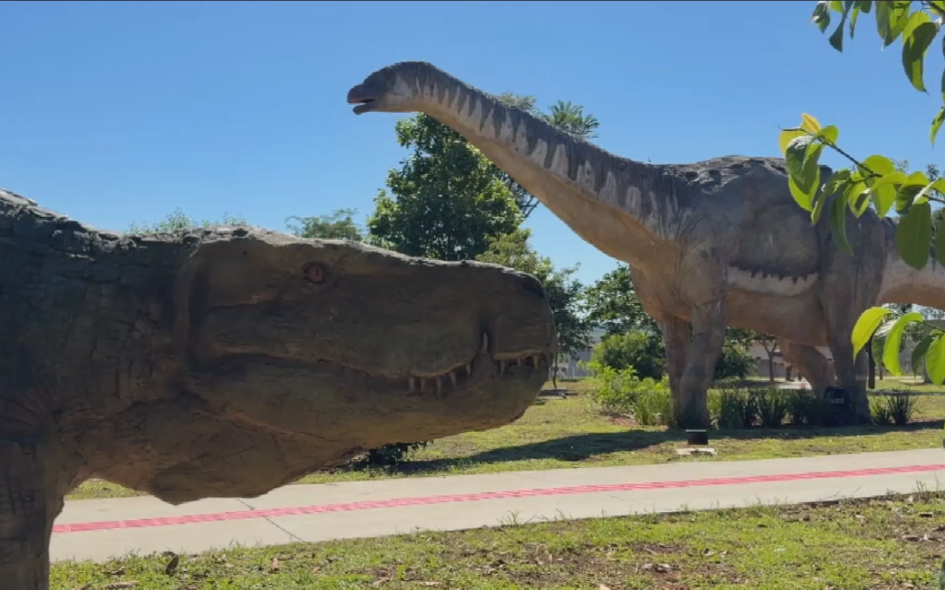 Crianças e adultos em frente a réplica de titanossauro no Parque dos Dinossauros de Uchoa