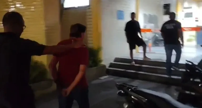 Idoso algemado sendo conduzido por policiais em frente a um shopping no Rio de Janeiro.