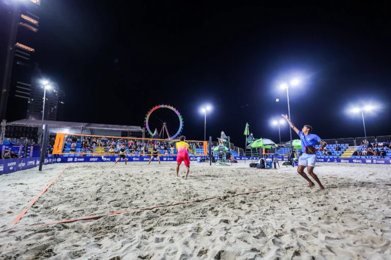 Quadra de beach tennis com atletas em jogo e público assistindo ao ITF BT400 em Balneário Camboriú