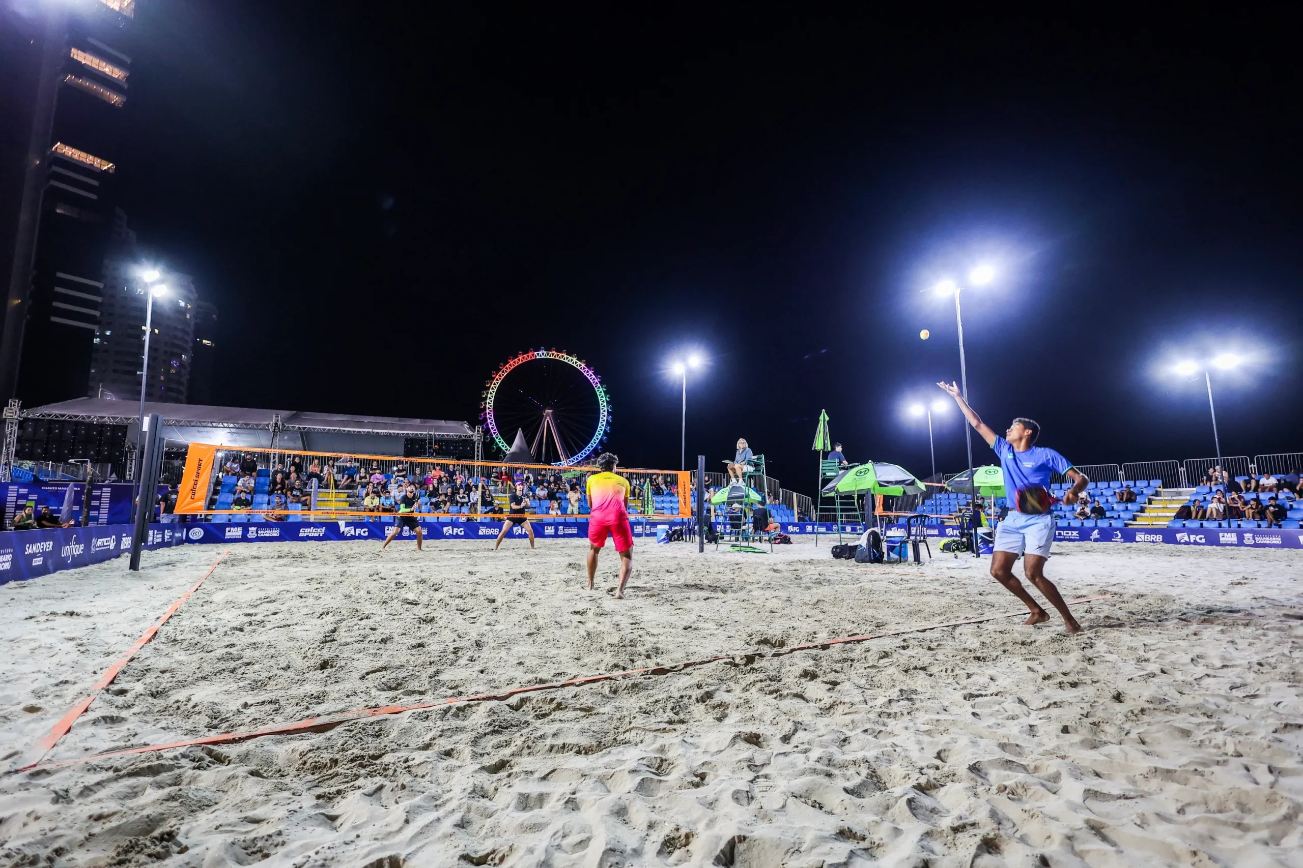 Quadra de beach tennis com atletas em jogo e público assistindo ao ITF BT400 em Balneário Camboriú