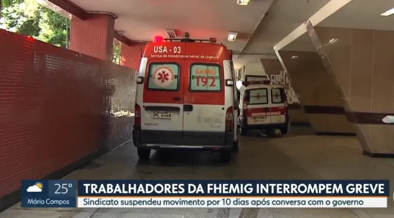 Grupo de trabalhadores da Fhemig em uniformes hospitalares, com cartazes, em frente a um hospital, simbolizando a suspensão da greve.