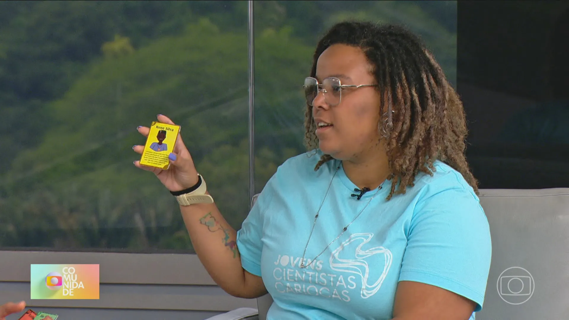 Thais Dias Xavier, mulher negra, segurando uma carta do seu jogo de combate ao racismo com imagem de personagem negro