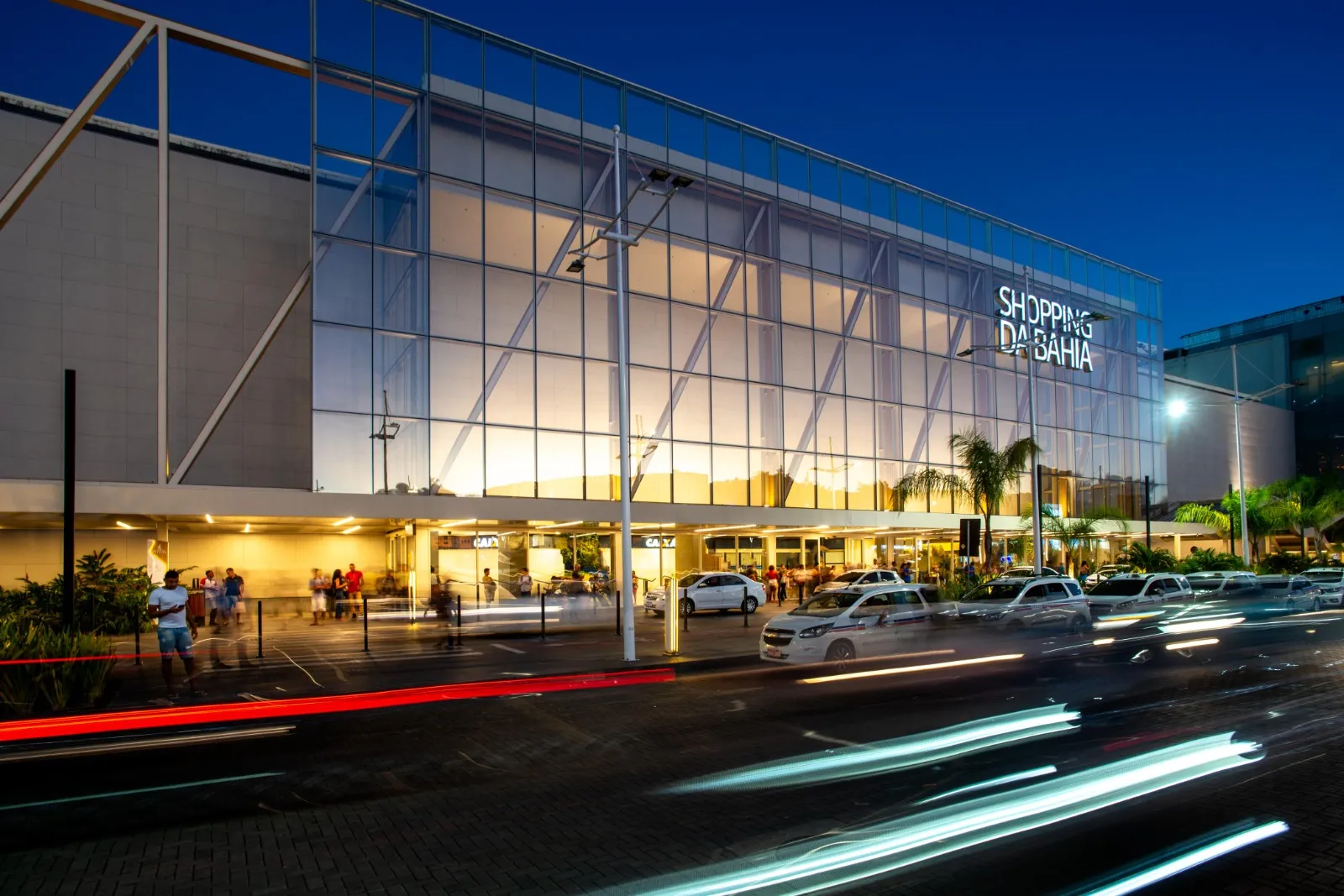 Pessoas em frente a um shopping de Salvador durante a Semana Santa, com informações de horários de funcionamento.