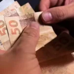 Mãos segurando celular com app Carteira de Trabalho Digital e informações do Abono Salarial PIS/Pasep 2026.