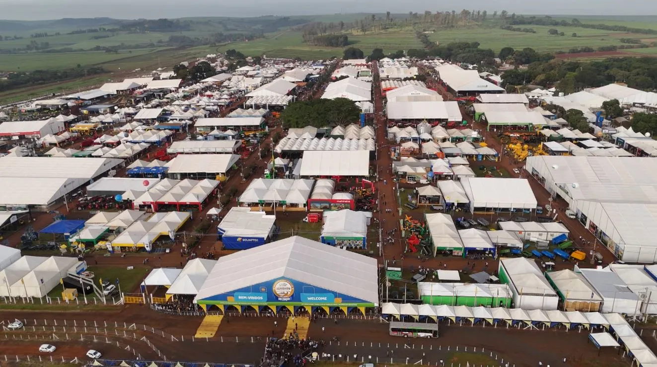 Vista panorâmica da Agrishow, com tratores, colheitadeiras e estandes ocupando uma grande extensão de terreno.