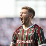 Jogadores do Fluminense comemorando um gol em campo, com o placar de 3 a 2 ao fundo, durante partida contra o Santos.