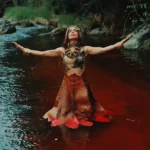 Anitta meditando em meio à natureza, com referências a sua fé no Candomblé e outras práticas espirituais.