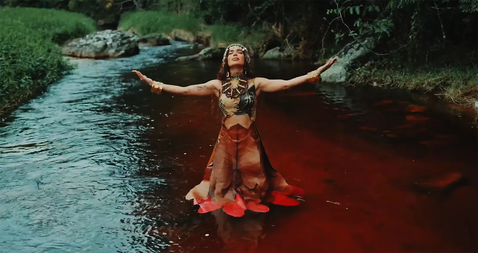 Anitta meditando em meio à natureza, com referências a sua fé no Candomblé e outras práticas espirituais.