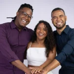 Trio de baianos criadores da ferramenta de IA Yá, sorrindo e celebrando em palco de conferência internacional.