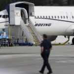 Linha de montagem da Boeing com trabalhadores montando peças de avião sob iluminação clara.