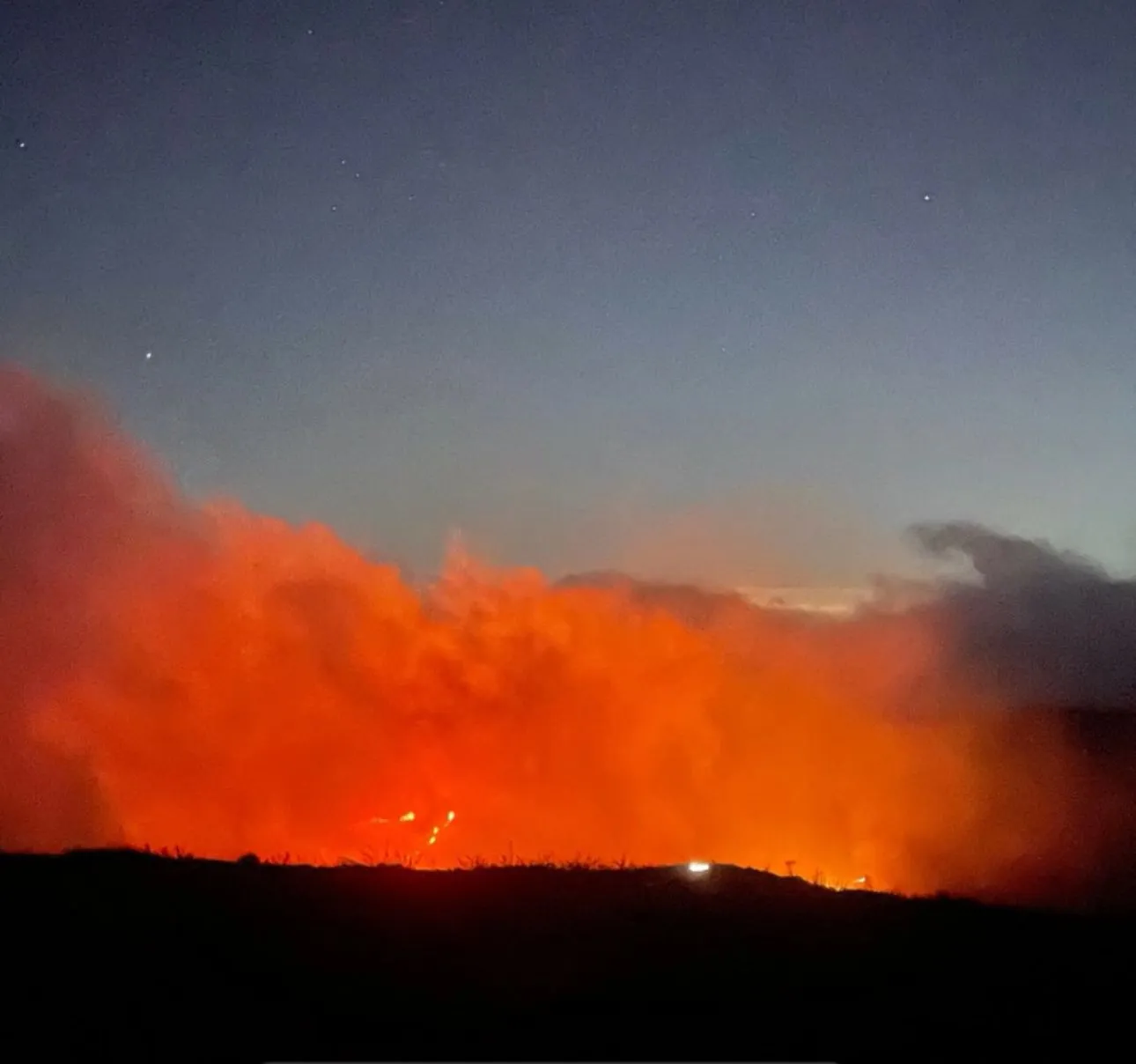 Bombeiros combatendo incêndio florestal no Morro do Açu, Parque Nacional da Serra dos Órgãos, com fumaça e paisagem montanhosa ao fundo.
