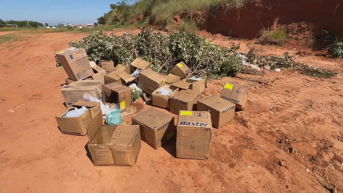Materiais médicos descartados ilegalmente em rua de terra em Bauru, SP, mostrando seringas e caixas de medicamentos.