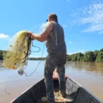 Pescador artesanal lançando rede, com referência à legislação do seguro-defeso