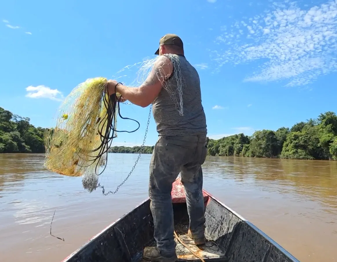 Pescador artesanal lançando rede, com referência à legislação do seguro-defeso