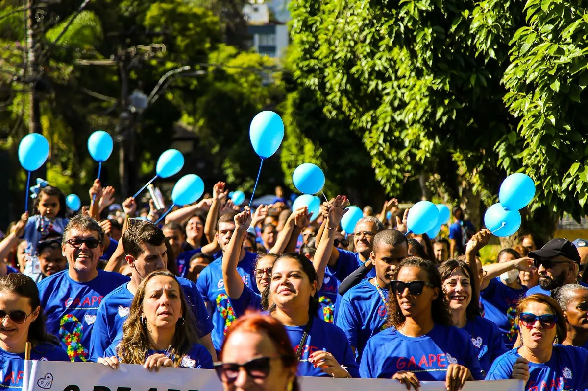 Grupo de pessoas caminhando em Petrópolis, com camisetas azuis, em evento de conscientização sobre autismo.