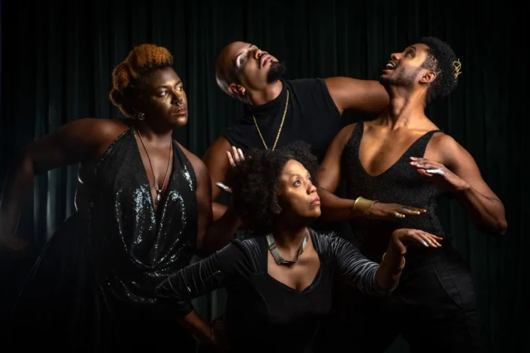 Pessoas assistindo a uma peça teatral em palco externo no Campo das Artes, com o sol se pondo e natureza exuberante.
