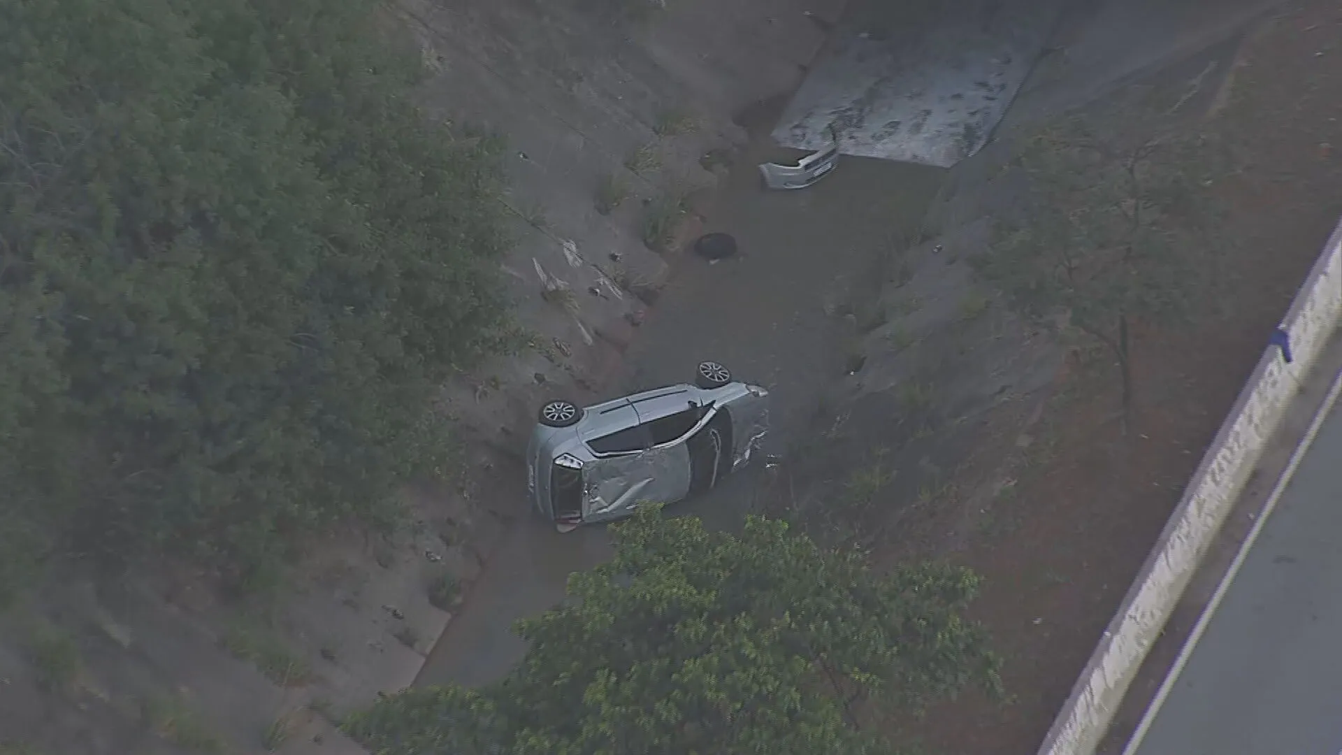 Carro capotado e parcialmente submerso em córrego na Avenida Jacu-Pêssego, com bombeiros e polícia no local.