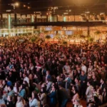 Pessoas em festival gastronômico 'Seu Mercado' em Juiz de Fora, com palco e barracas de comida