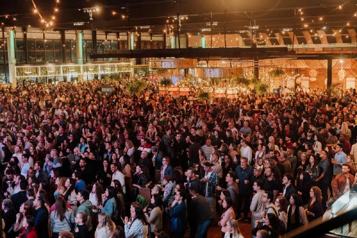 Pessoas em festival gastronômico 'Seu Mercado' em Juiz de Fora, com palco e barracas de comida