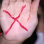 Mão feminina com X vermelho, símbolo global contra a violência doméstica em São Paulo