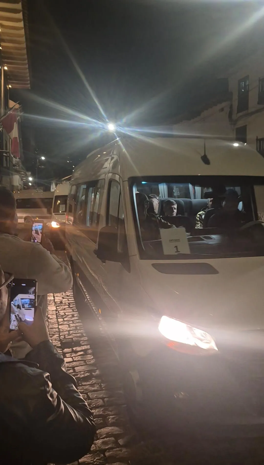 Jogadores do Flamengo desembarcando de vans em Cusco, Peru, à noite, em meio a torcedores e arquitetura colonial.
