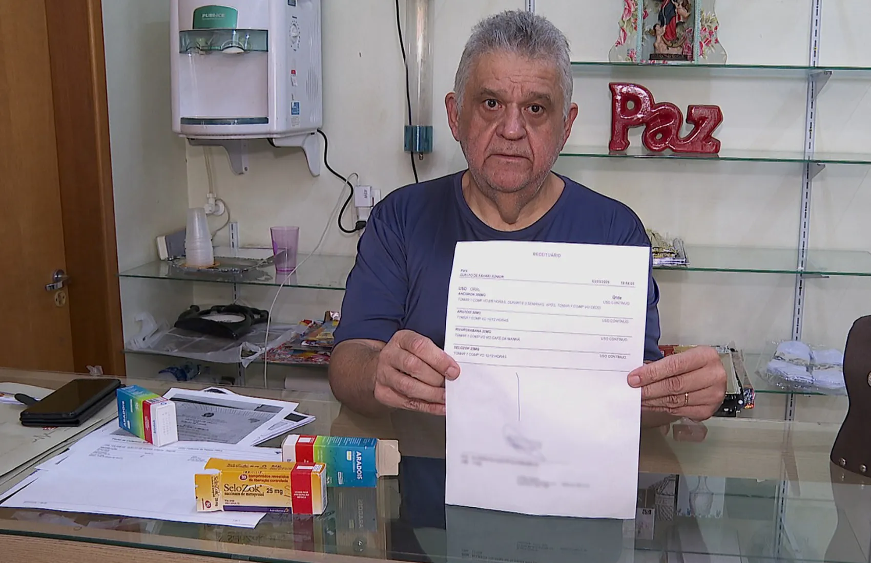 Homem idoso confuso em farmácia, tela de computador com erro 'CPF cancelado por óbito' do SUS