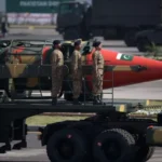 Imagem de uma explosão nuclear simulada no horizonte com figuras observando, representando a ameaça da corrida nuclear