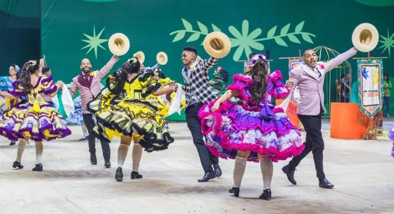 Dançarinos de quadrilha com trajes típicos e cenários dos enredos no Arraial de Belô 2026