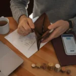 Mãos com calculadora e notas, redes sociais ao fundo, simbolizando gerenciamento de dívidas