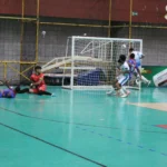 Partida de futsal da Copa TV Grande Rio, jogadores disputando a bola em quadra, placar eletrônico ao fundo.