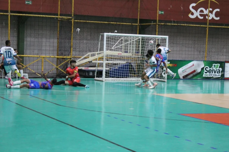 Partida de futsal da Copa TV Grande Rio, jogadores disputando a bola em quadra, placar eletrônico ao fundo.