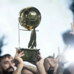 Troféu verde da Copa Verde com fundo de campo de futebol