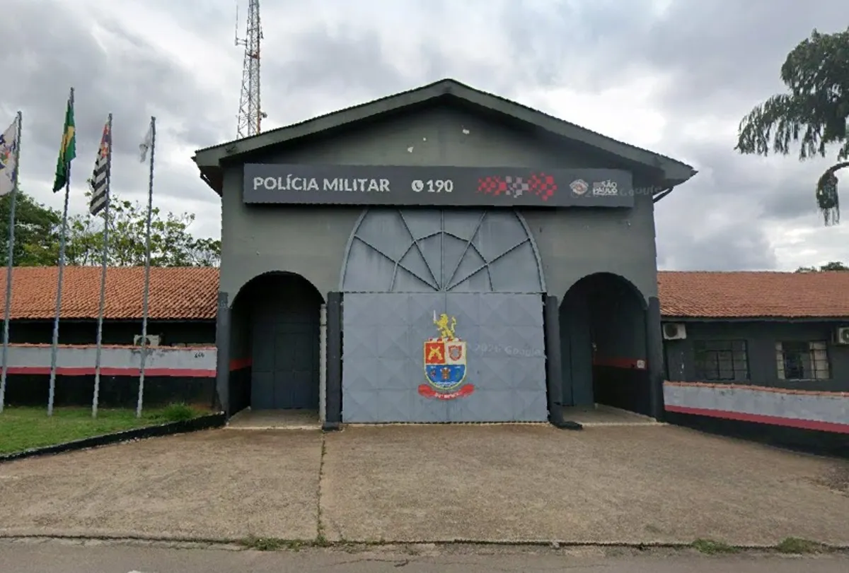 Insígnia da PM, notas de dinheiro e algemas sobre mesa, indicando corrupção.