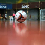 Partida de futsal da Copa TV Grande Rio com jogadores em movimento e bola em destaque