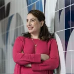 Julia Quinn, autora de Bridgerton, sorrindo e autografando livros para fãs em um estande na Bienal do Livro Bahia.