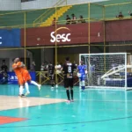 Dois jogadores de futsal disputando a bola em quadra, com um deles finalizando para o gol, durante a Divisão Especial Futsal.