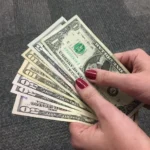 Notas de dólar com mapa-múndi e gráficos financeiros ao fundo