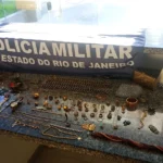 Bolsa aberta cheia de joias (anéis, brincos, pulseiras) sendo inspecionada por um policial.