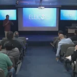 Estúdio de TV com logo Eleições 2026 e cadeiras para candidatos