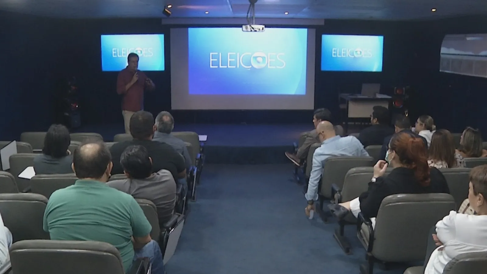 Estúdio de TV com logo Eleições 2026 e cadeiras para candidatos