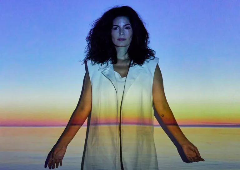 Cantora Emanuelle Araújo no palco, com figurino vibrante, expressando a energia da música afro-baiana de seu álbum 'Corra para o mar'.