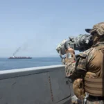 Soldado americano em navio de guerra observando embarcação iraniana em bloqueio