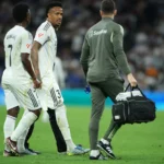 Éder Militão, jogador do Real Madrid, com uniforme branco e preto, correndo no gramado durante jogo.