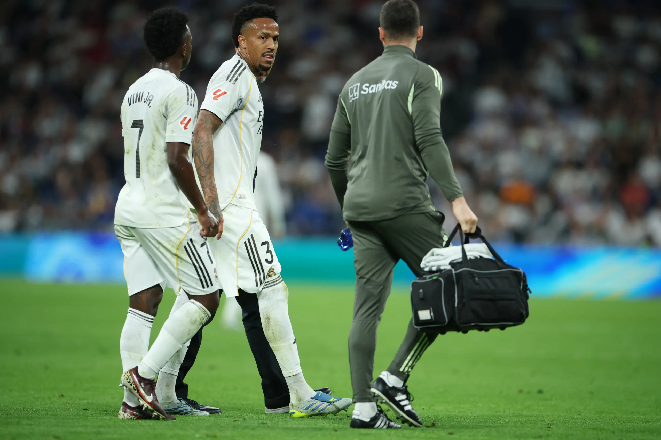 Éder Militão, jogador do Real Madrid, com uniforme branco e preto, correndo no gramado durante jogo.
