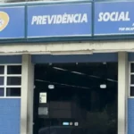 Pessoas esperando em uma fila com telas de computador mostrando erros, representando as falhas no INSS e o impacto nos processos.