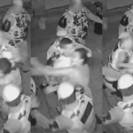 Dois policiais militares entrando em uma casa à noite, capturados por câmera de segurança, enquanto um membro da família observa a invasão.