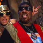 Fernanda Abreu e Afrika Bambaataa no set de 'Tambor', com tambores e cenário de favela carioca.
