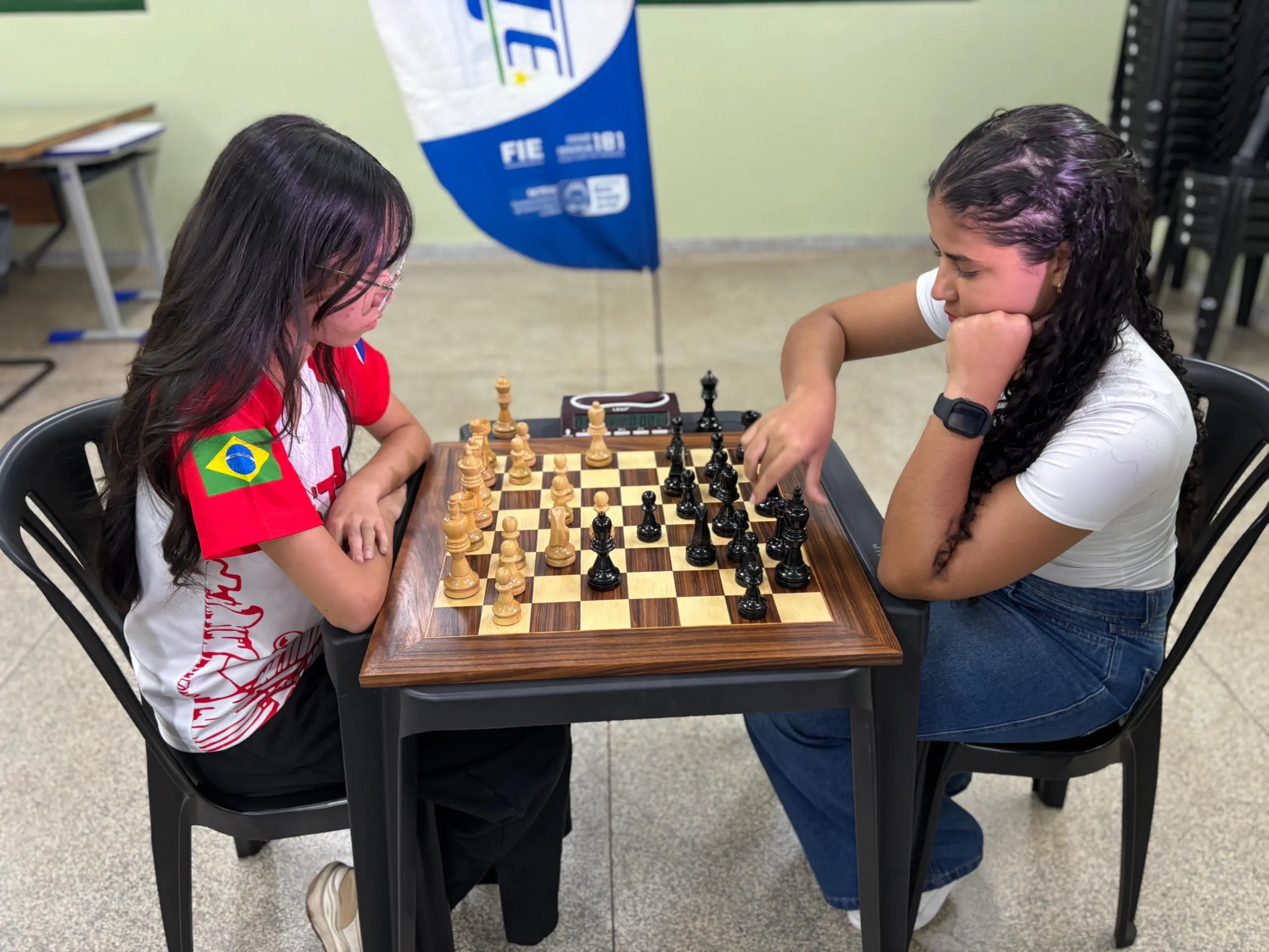 Alunos de todas as idades jogando xadrez em Campo Grande, com foco nas peças e no tabuleiro, durante as aulas gratuitas da Fundesporte.
