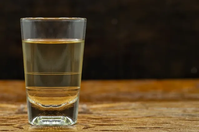 Garrafa de cachaça em ambiente rústico, com sugestão de perigo e contaminação por 'chumbinho'.